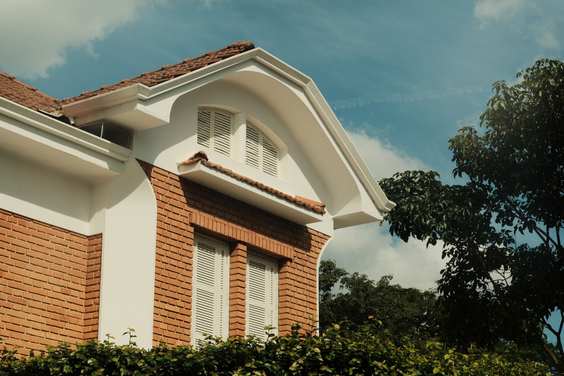 Exterior shot of a brick house featuring an arched roof and white shutters, set against a blue sky.